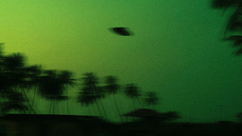 silhouette of UFO and palm trees against a green sky