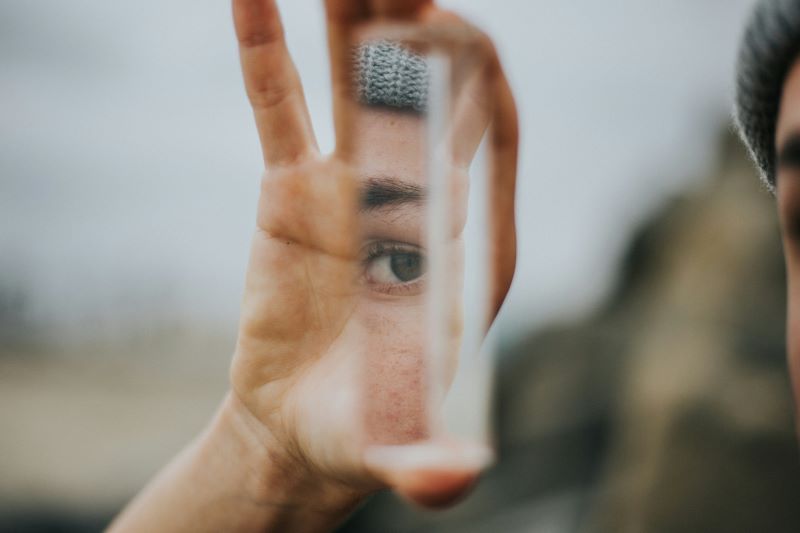 a hand holding a small mirror that's reflecting a woman's eye