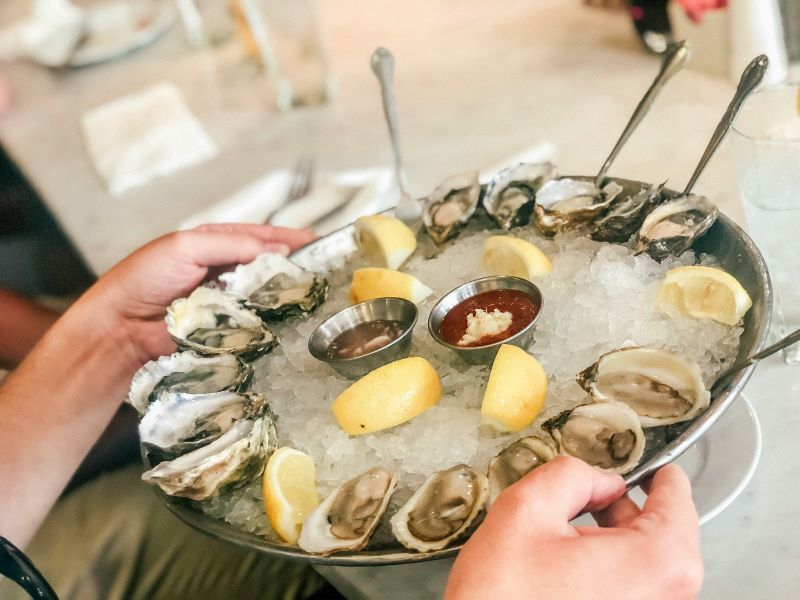 hands holding a plate of oysters on ice